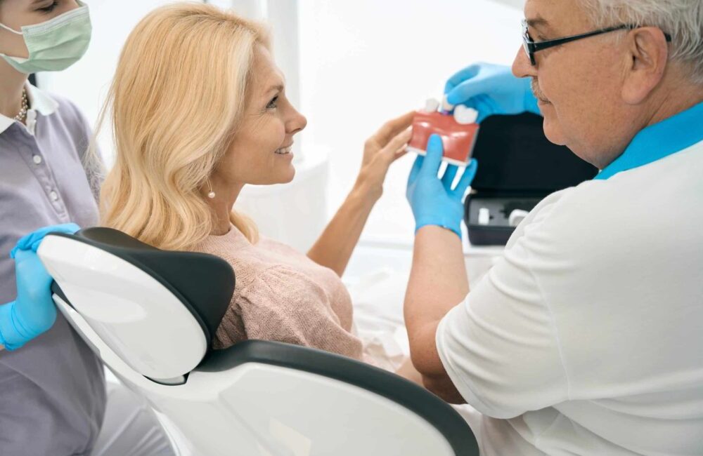 Dentist,Holding,Model,Of,Teeth,With,Dental,Implant
